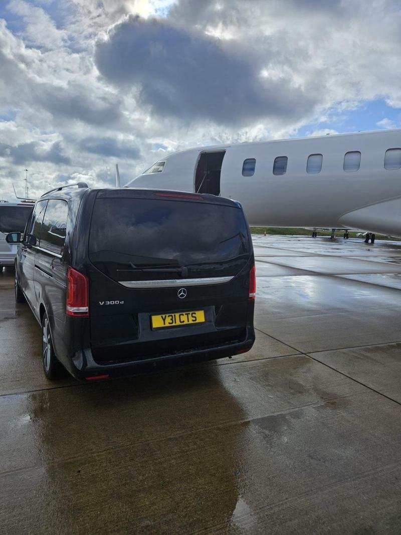Complimentary airport waiting time while a delayed flight lands Rear view of a chauffeur-driven Mercedes-Benz V-Class parked beside a private jet on a wet apron while waiting for a delayed arrival