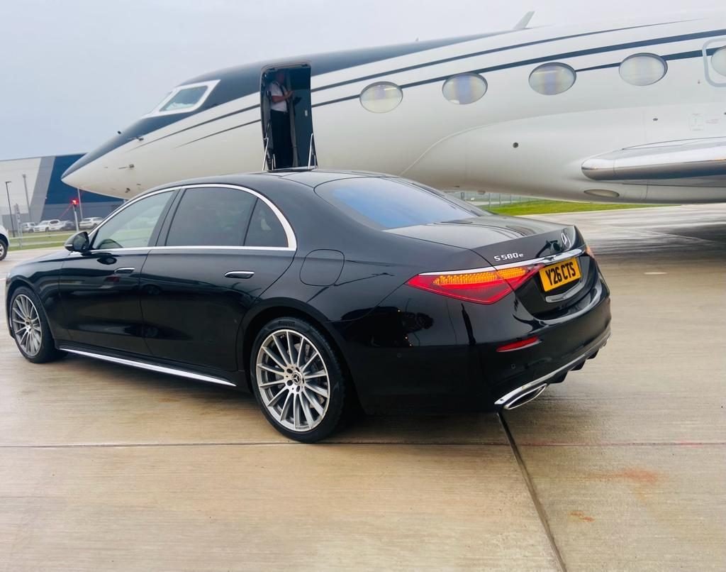 Black Mercedes-Benz S-Class chauffeur car waiting beside a private jet on the apron