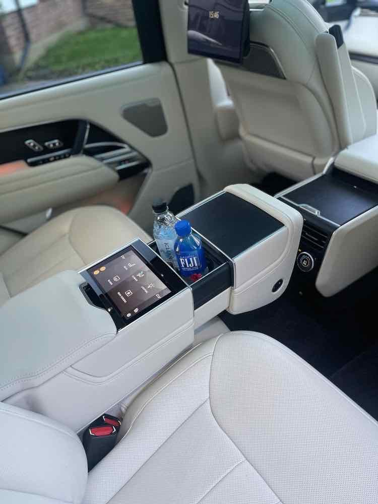 Rear cabin of a Range Rover chauffeur car with cream leather seats, rear climate controls and bottled water, ready for a Heathrow to Central London transfer